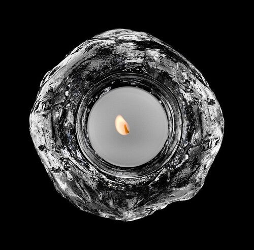 A textured, clear glass sphere tea light candle holder as seen from above with a lit candle in the hollow at its centre, sat against a black background.