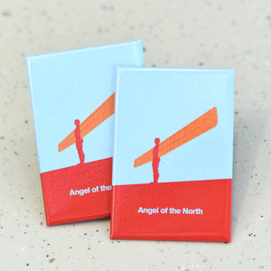 Two flat rectangle magnets sit one on top of the other - they feature a colourful, graphic illustration of a figure with large, flat, wings in shades of orange against a blue backdrop and red base. Within the red panel at the bottom, bold pale blue text reads "Angel of the North".
