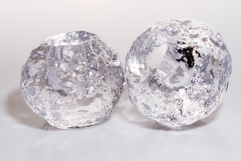 Two textured, clear glass sphere tea light candle holders, that resemble a melting ball of ice, sit beside each other against a white background.