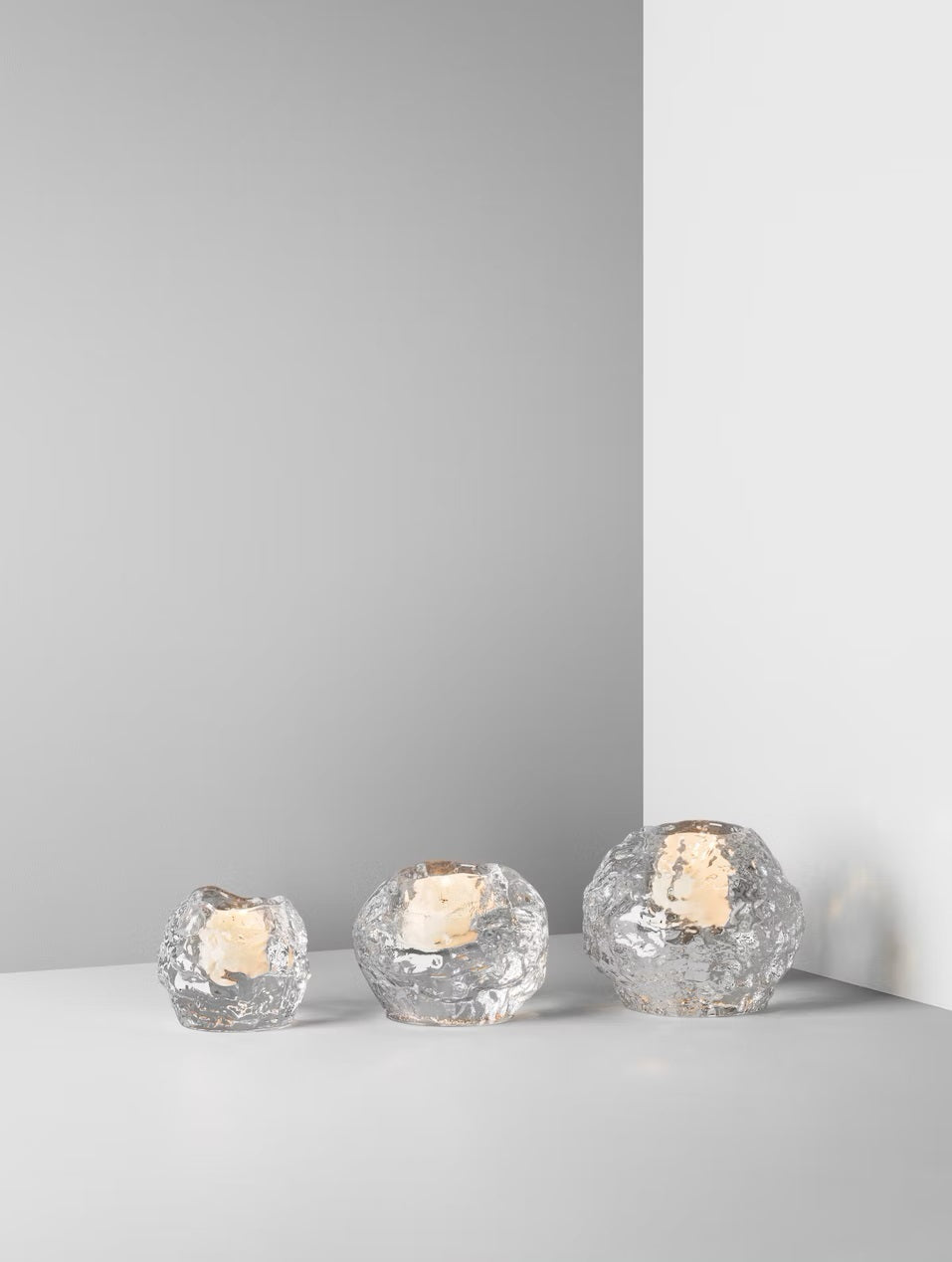 Three textured, clear glass sphere tea light candle holders sat in a line from smallest on the left and largest on the right against a white background.